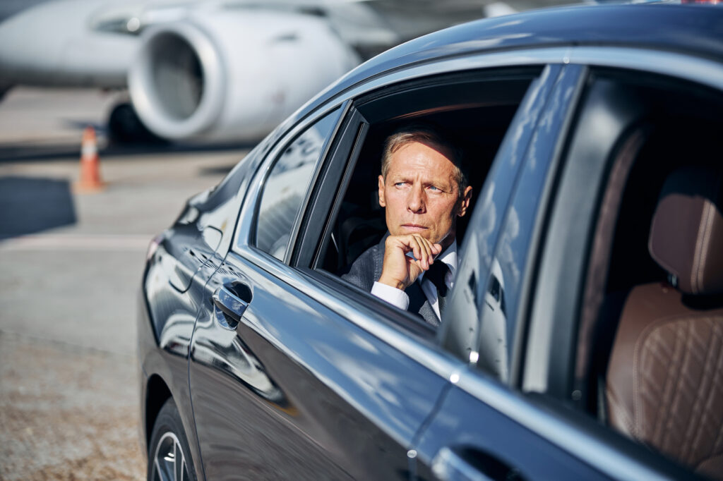 Serious businessman in suit is going by car on back seat after flying by plane to airport